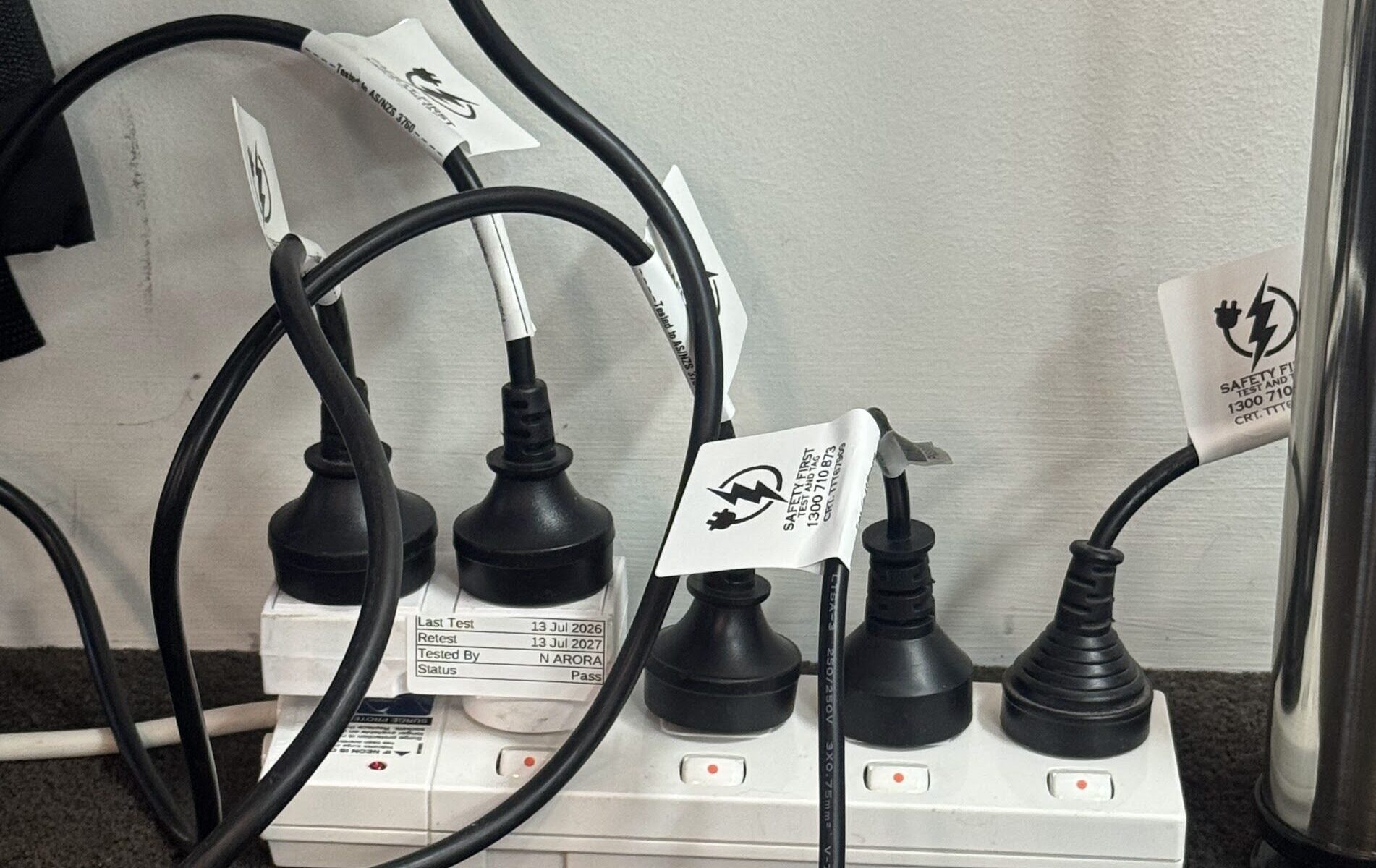 A power extension board and connected electrical leads displaying passed safety test tags after a successful electrical inspection.