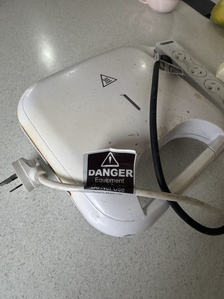 A broken kitchen toaster marked with a red out-of-service tag after failing an electrical safety test in an NDIS care facility.