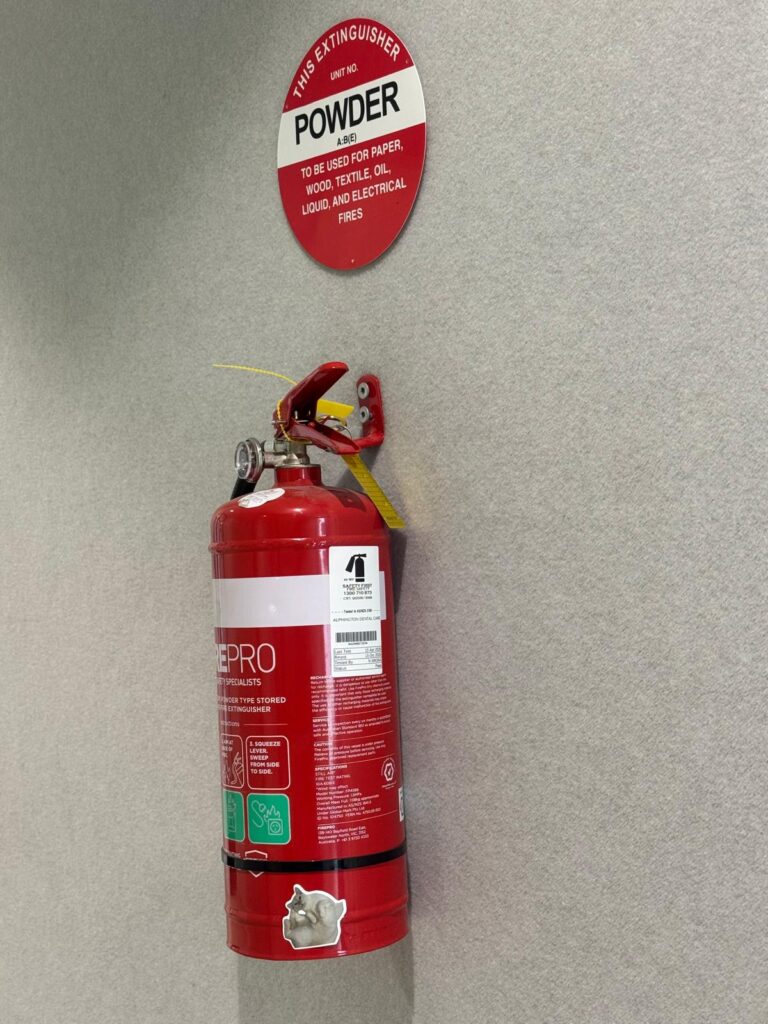 A Safety First technician performing an AS 1851 fire extinguisher inspection and applying a metal punch tag in a commercial workplace.